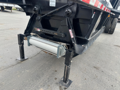 Dump trailer rear corner showing landing gear legs and hydraulic cylinder with label stickers.