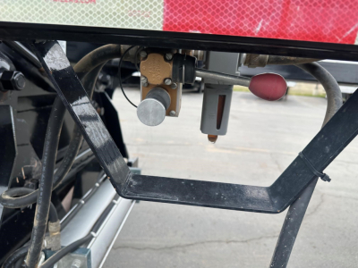 Trailer hitch area showing valve and lever components on Brazos bottom dump trailer, with a gray vertical handle and a red knob visible.