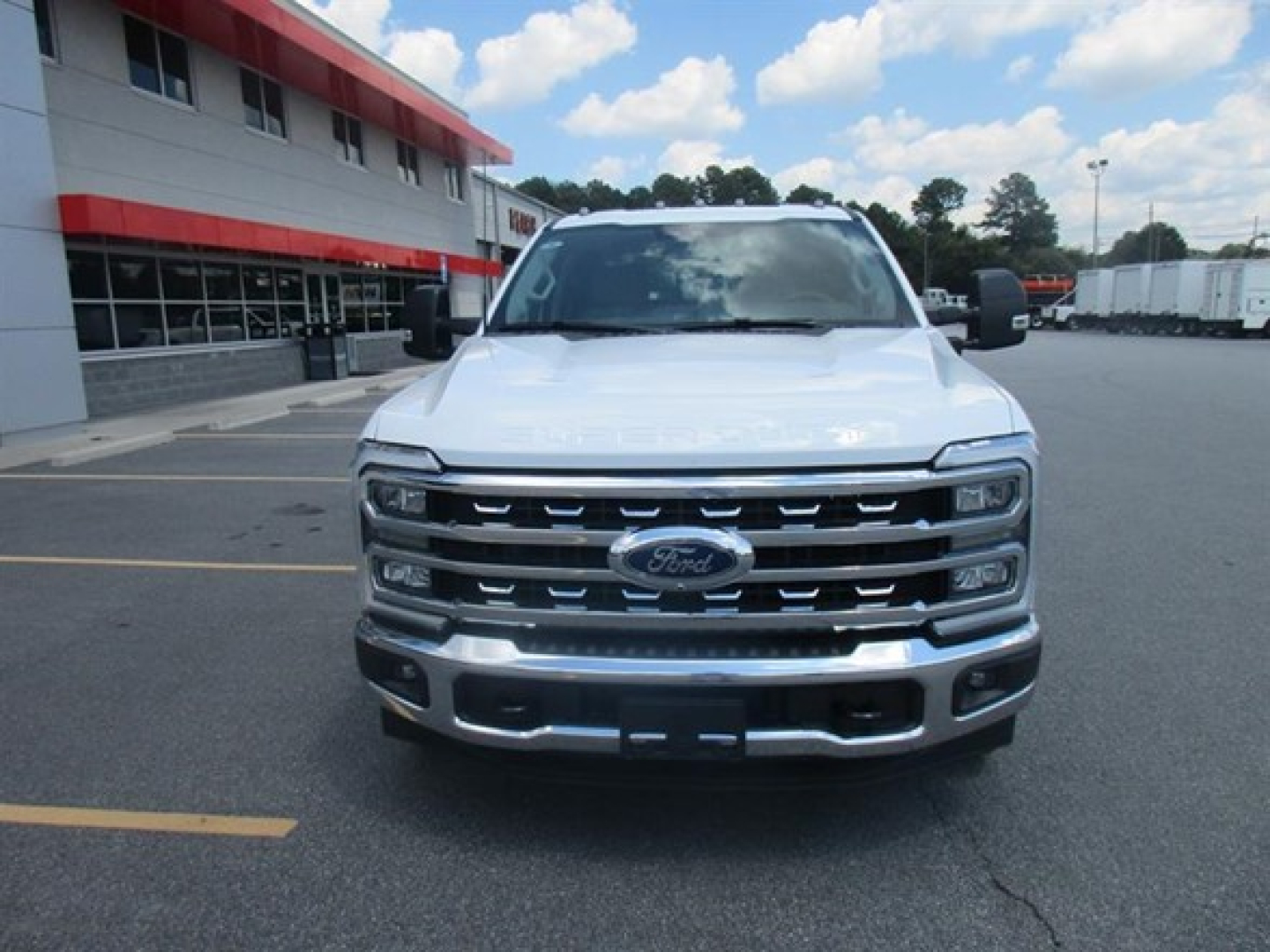 Front view of a white 2026 Ford F-250 pickup truck parked in a dealership lot, showing chrome grille with Ford emblem and headlights.