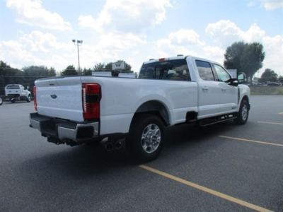 Ford F-250 pickup truck in a parking lot, rear and passenger side visible, white with crew cab, dual exhausts visible, dealership lot background.