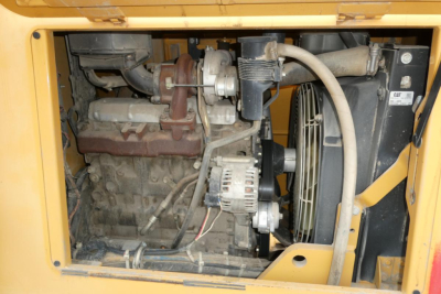 Engine compartment of a yellow lifted truck or lift showing engine, alternator, belts, and cooling fan. Visible components include alternator, radiator fan shroud, exhaust manifold, and various hoses and wiring.