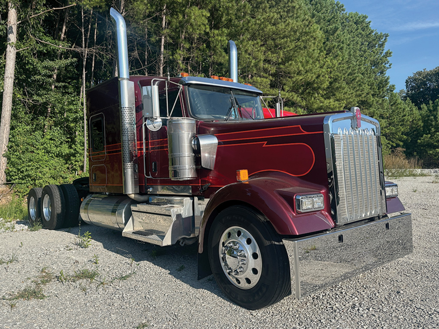 Kenworth W-900L AeroCab tractor in maroon with chrome exhaust stacks, grille, and dual rear axles, front view on gravel lot.