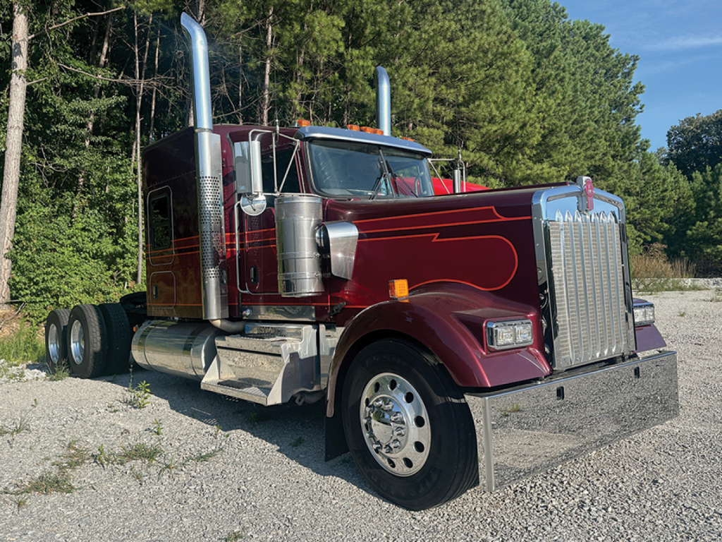 Kenworth W-900L AeroCab tractor in maroon with chrome exhaust stacks, grille, and dual rear axles, front view on gravel lot.