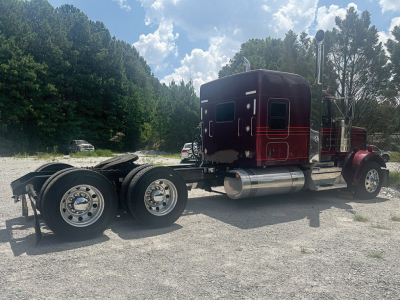 Kenworth W-900L AeroCab tractor with maroon cab, chrome fuel tanks, and dual rear axles in a gravel lot.