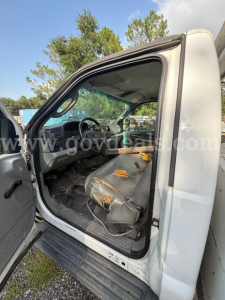 Ford F-550 cab interior view from driver's side with bench seat, worn upholstery, and open door; steering wheel, dashboard, and floor mats visible.