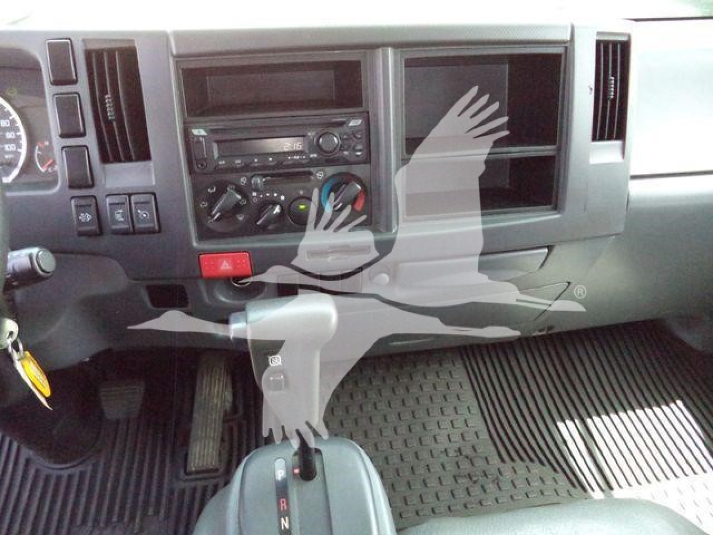 Dashboard and center console of a 2019 Isuzu NPRR flatbed dump truck interior with gear shifter, radio, and climate controls.