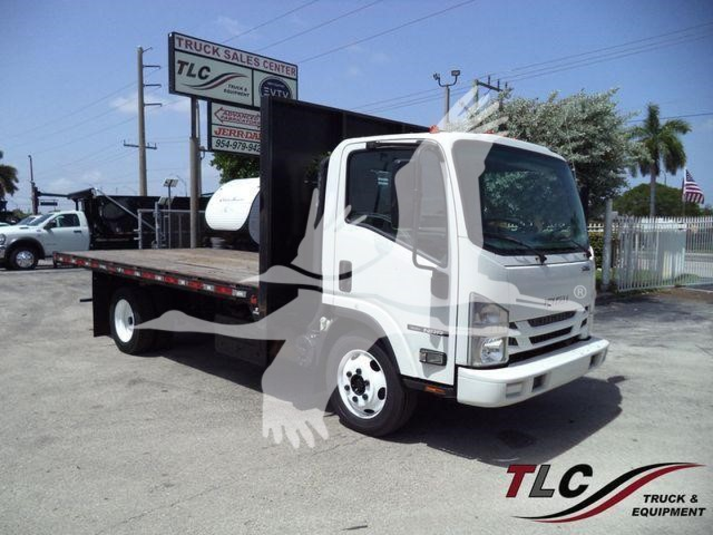Isuzu NPR/NRR flatbed dump truck with white cab and long black flatbed, dealership sign in background, TLC Truck Sales Center watermark.