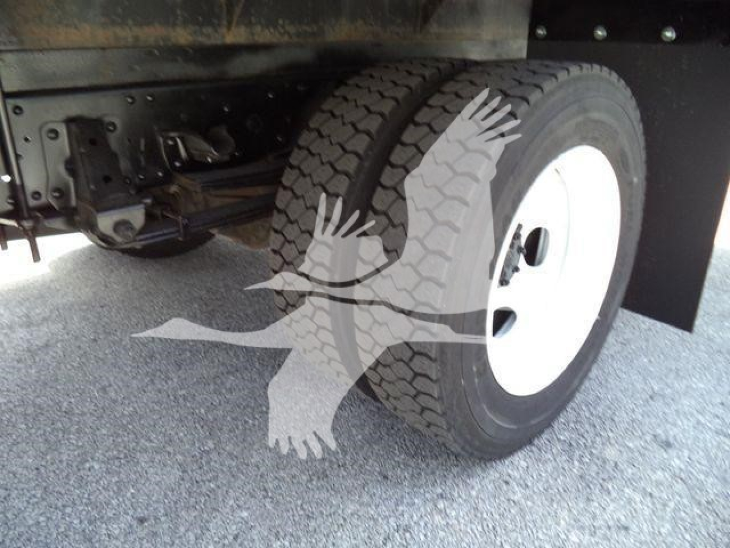 Isuzu truck wheel and undercarriage view showing dual rear wheels and white rim; underbody components visible.