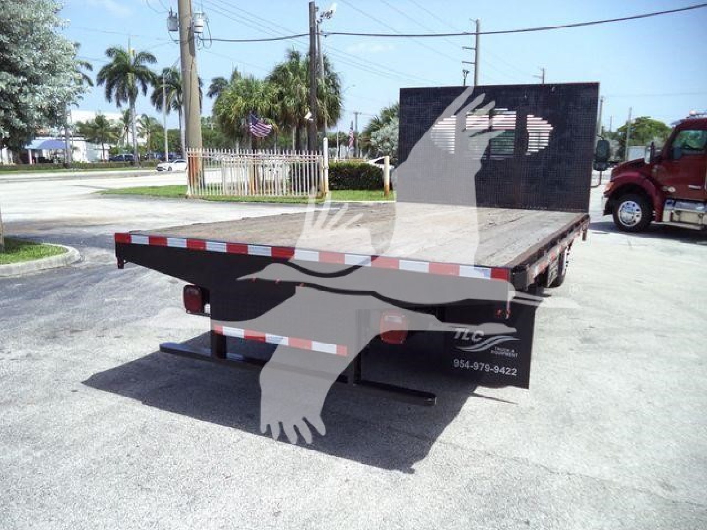 Isuzu NPR flatbed dump truck rear view showing flatbed with reflective stripes and rear underride guard.