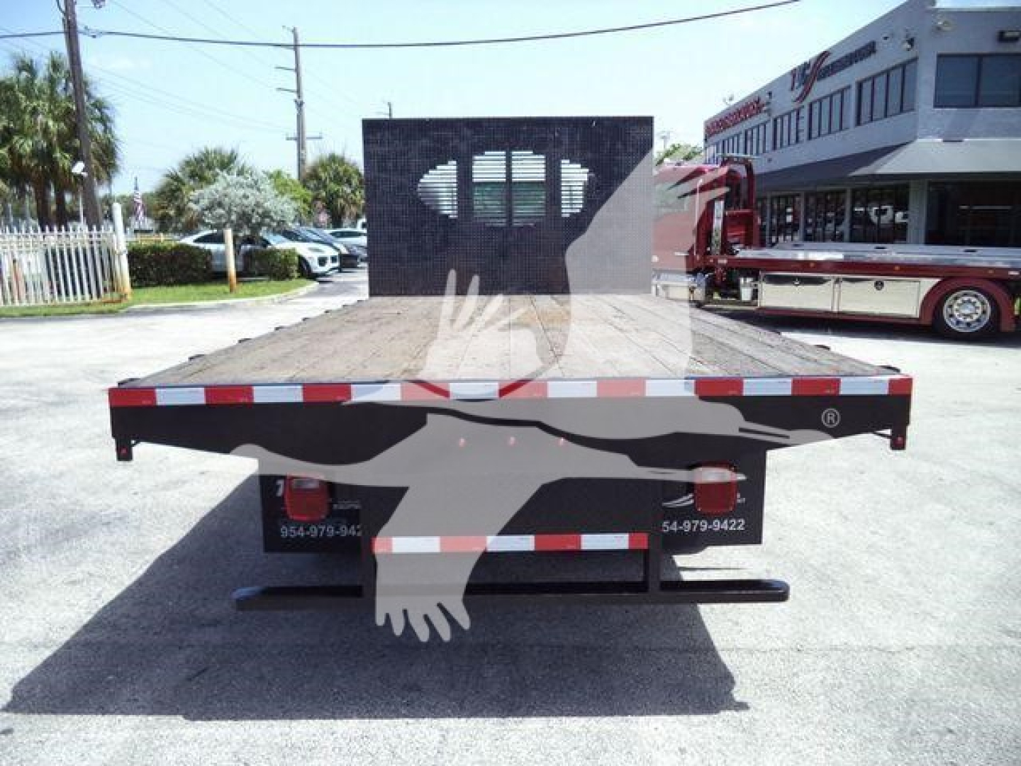 Isuzu flatbed dump truck rear view showing flatbed with reflective red/white stripes and rear bumper, eagle watermark overshadowing.
