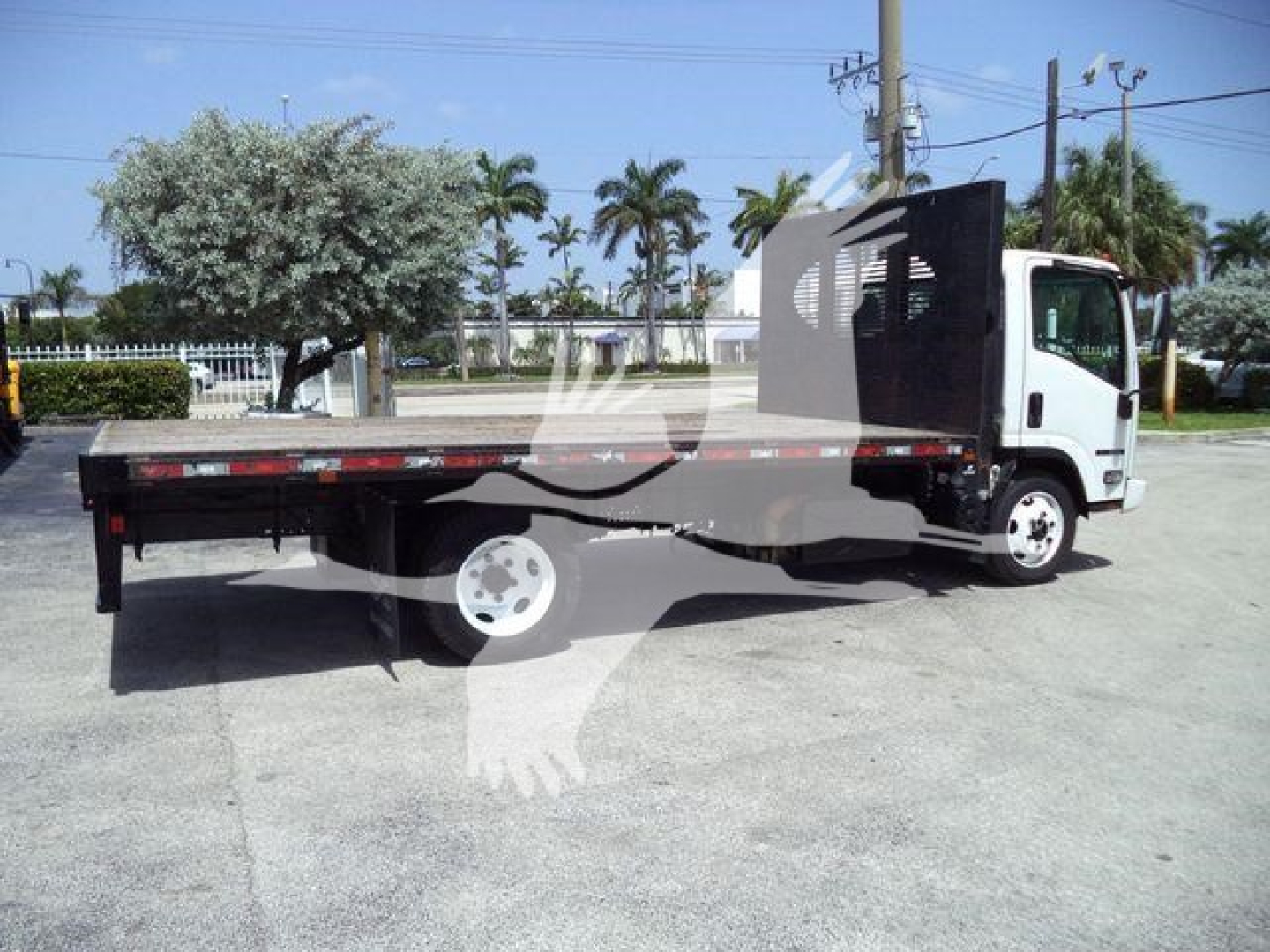 Isuzu NPR flatbed dump truck side view showing flatbed cargo area and cab, JALE5W165K7300722 VIN plate visible (image with palm trees).