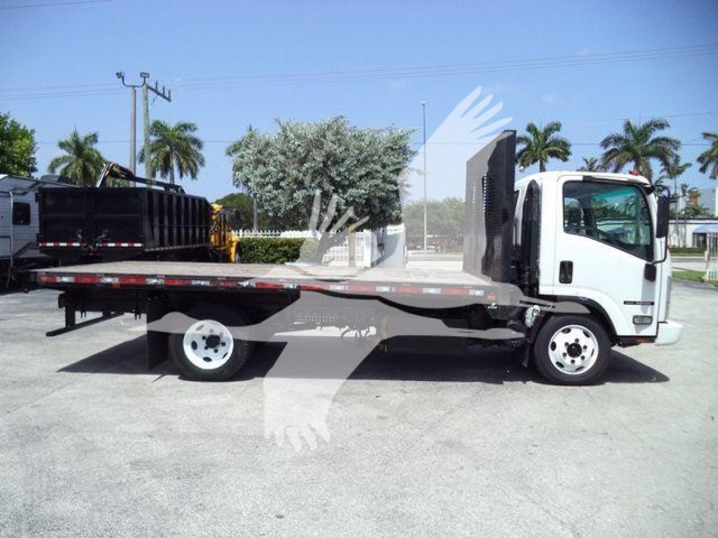Isuzu NRR flatbed tow truck side view showing flatbed bed with loading ramps and dual rear wheels.