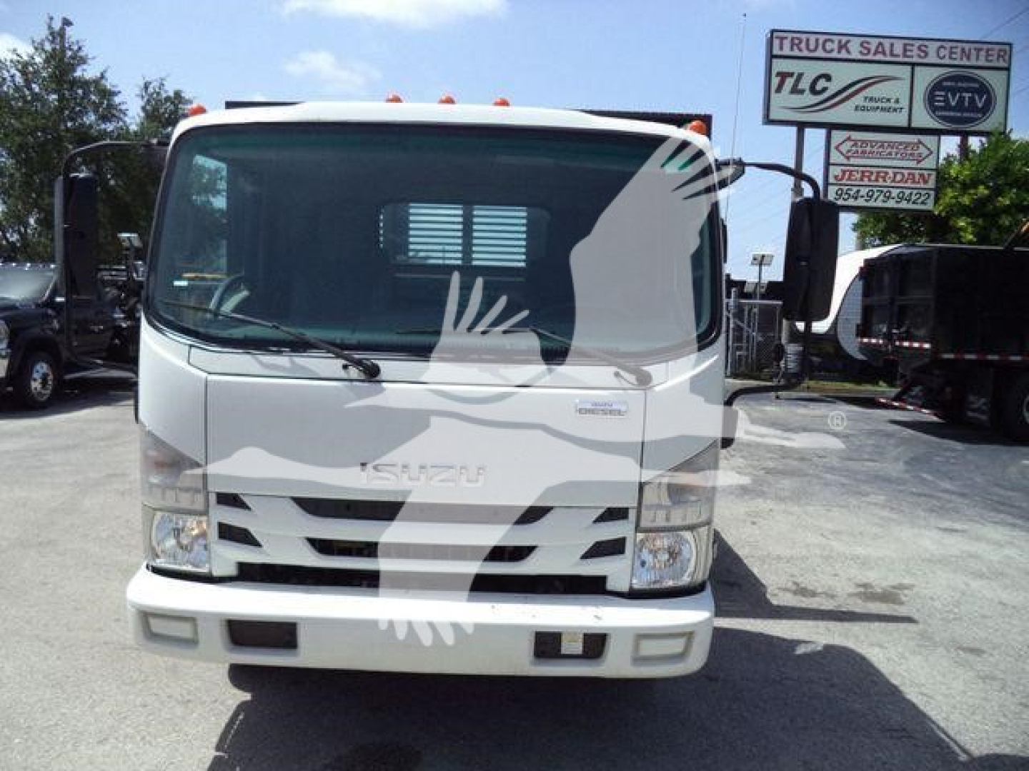 Isuzu NRR flatbed dump truck front view with grille, headlights, and windshield. Window reflection shows a white silhouette overlay. Text on truck not legible from distance.