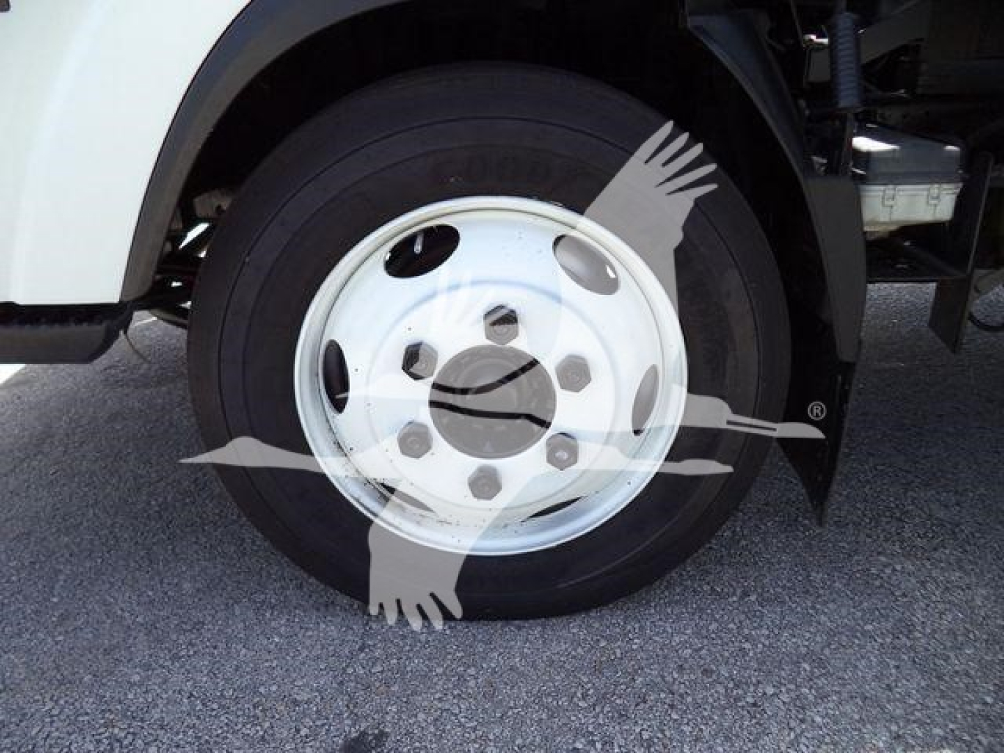 Isuzu truck front wheel and fender view showing steel wheel, tire, and part of flatbed dump undercarriage