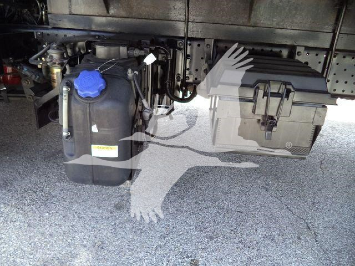 Underbody view of a 2019 Isuzu NRR truck showing a blue-capped coolant reservoir and a black plastic toolbox with metal latches.