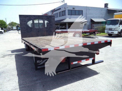 Flatbed dump truck bed on Isuzu NPR flatbed with open rear, metal deck, and black partition screen; orange and white reflective tape along edges; truck yard in background.