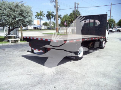 Isuzu NRR flatbed dump truck from rear-left view with flatbed, cab, and wheel. Visible text includes none clearly readable on this angle.