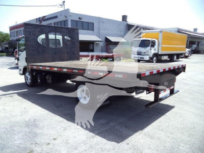 Isuzu flatbed dump truck in a dealership lot with a yellow box truck in background; flatbed has black screen divider and rear ramps.