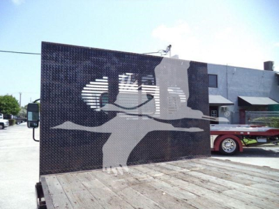 Flatbed dump truck bed seen from rear with diamond plate wall and silhouette graphic of a person lifting a load; blue building in background.