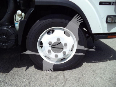 Isuzu NRR front wheel and fender showing wheel cover and partial cab with Isuzu badge; flatbed dump truck in light color.