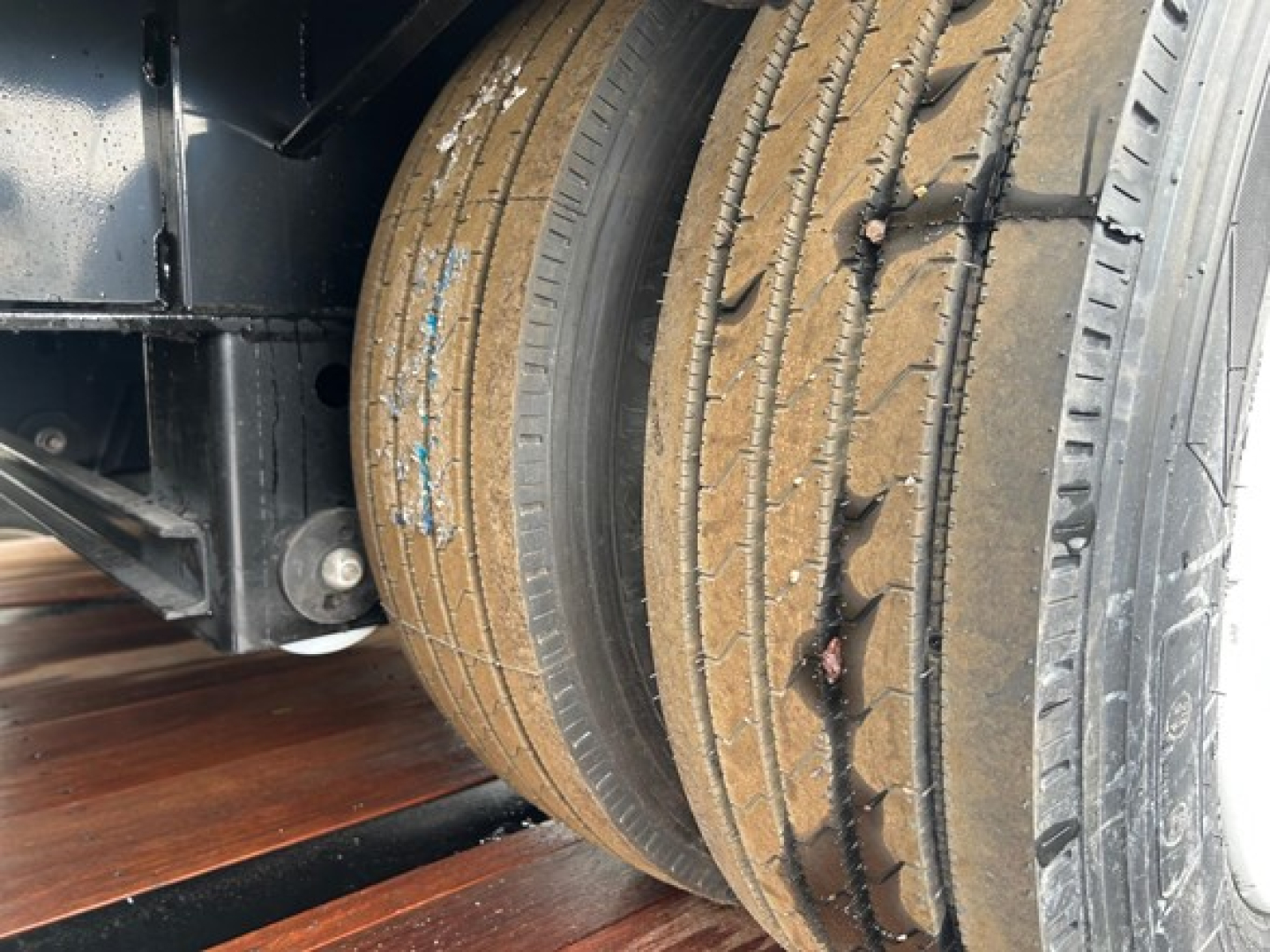 Trailer wheel and part of drop deck chassis with dual tires in view; visible tire treads and mud/dirt on tire surface.
