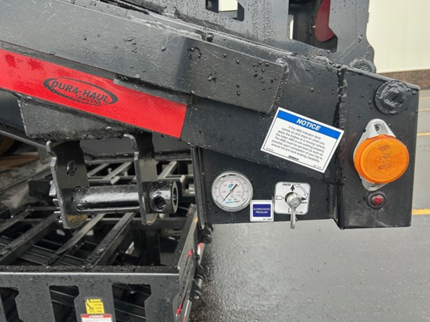Trailer rear section showing DURA-HAUL logo, gauges, orange safety light, label, and warning sticker on a drop deck trailer.