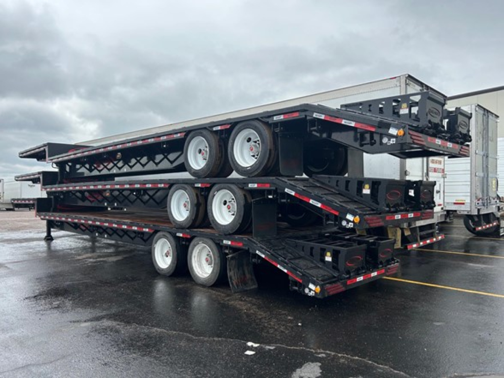 Trailer stack showing multiple drop decks with tandem axles and wheels, carrying a beaver tail design; 2026 Dura Haul Beaver Tail Drop Deck in a parking lot.
