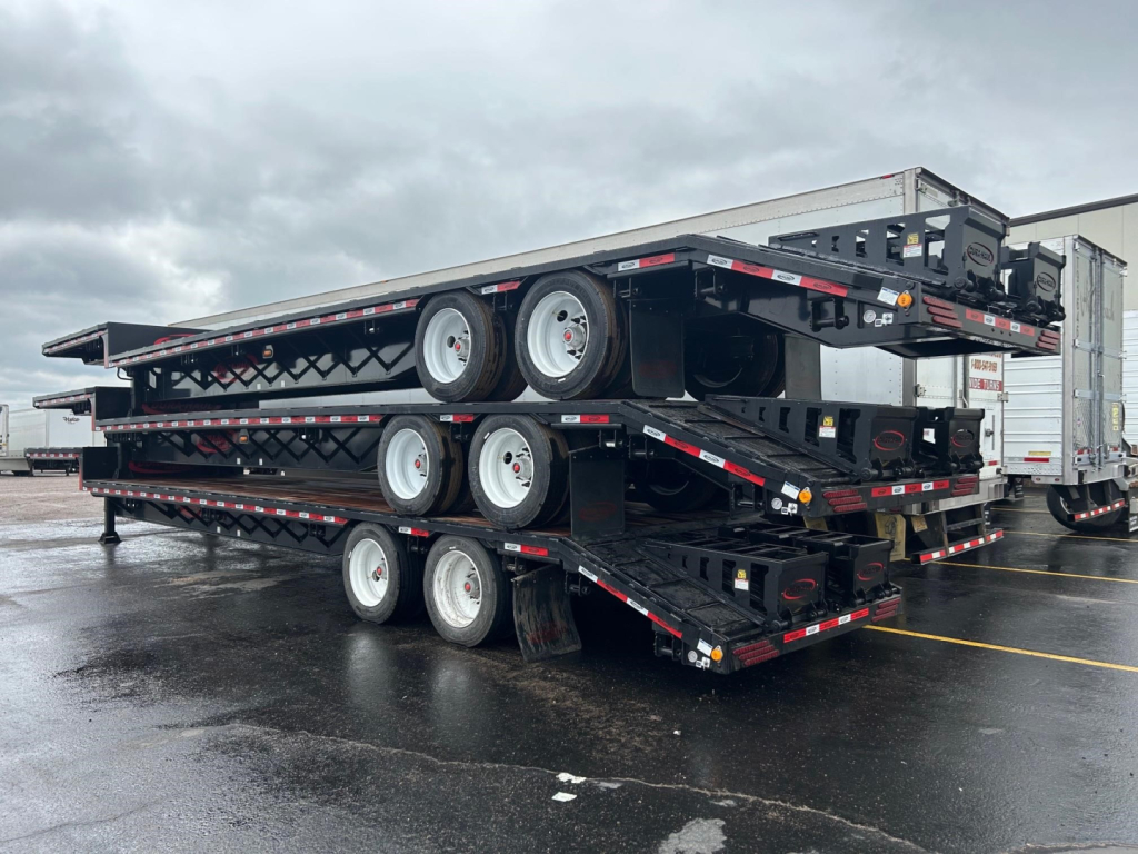 New 2026 Dura Haul Beaver Tail Drop Deck trailers stacked in a lot showing triple-axle beavertail configuration and steel deck with wheels.