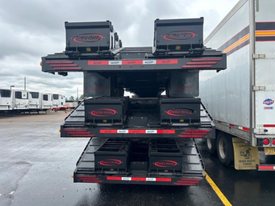 Fully stacked beavertail drop deck trailer with multiple storage boxes labeled CURTIS-HAIRED on each level, rear view showing three deck tiers.