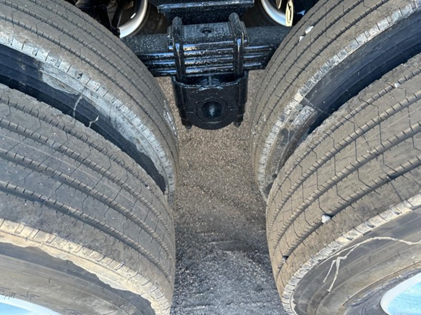 Trailer axle view showing dual rear tires and suspension components under a dump trailer.