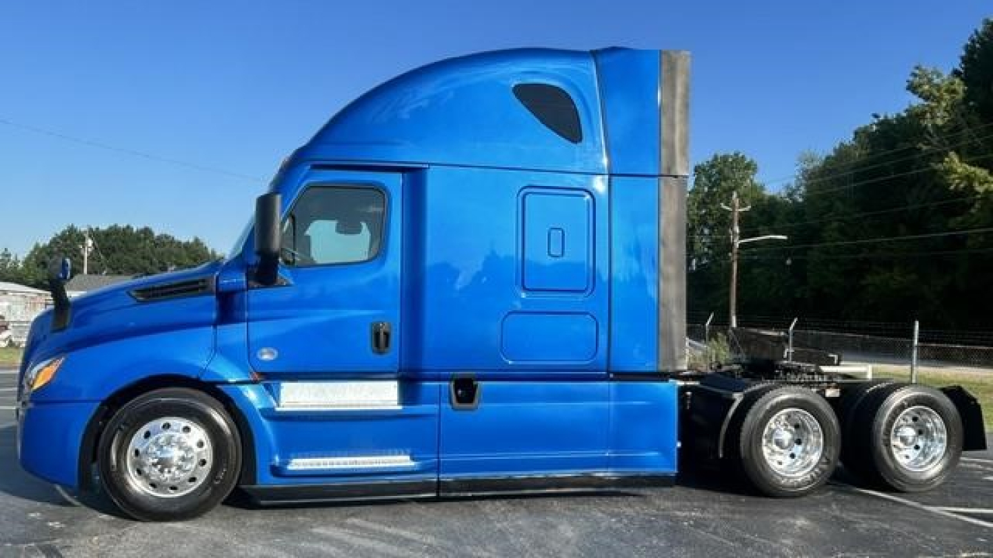 Truck side view of a blue 2022 Freightliner Cascadia 126 sleeper with chrome wheels and dual rear axles.