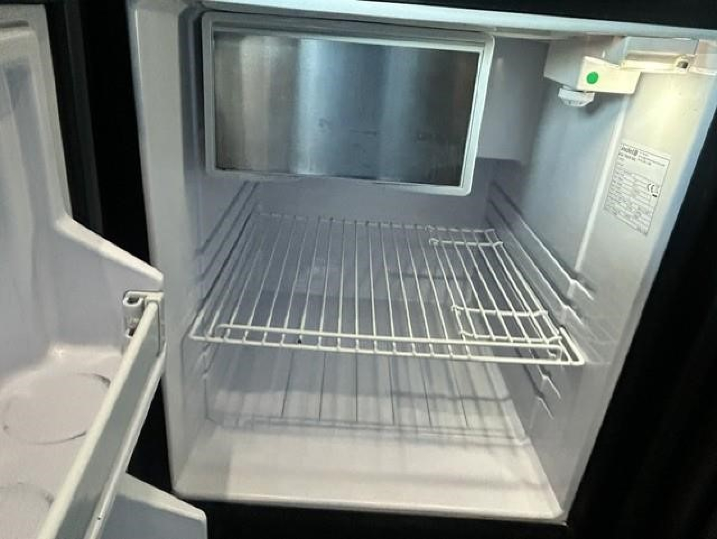 Freightliner Cascadia cab refrigerator/freezer interior view with empty freezer shelf in open compartment.