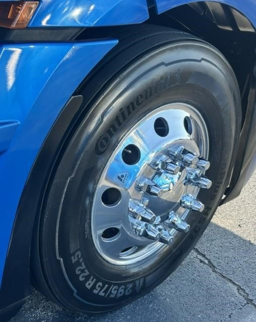 Wheel close-up on blue Freightliner Cascadia 126 truck showing Continental tire with chrome hub and lug nuts.