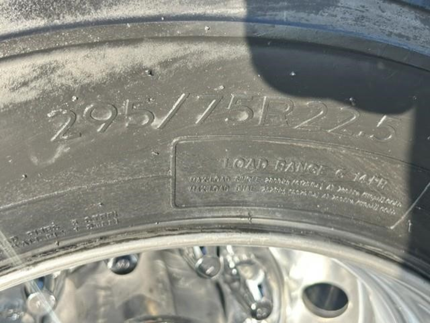 Tire sidewall with raised numbers 295/75R22.5 and a blank rectangular stamp area with serial text, part of wheel and rim visible.