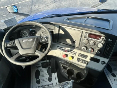 Truck cab interior of a Freightliner Cascadia 126 showing steering wheel, dashboard, control panels, and cup holders.