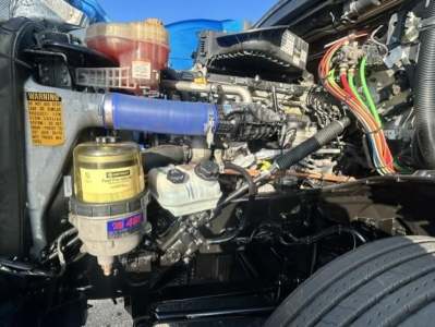 Freightliner Cascadia 126 engine bay showing blue intercooler hose, various fluid reservoirs, wiring, and components.