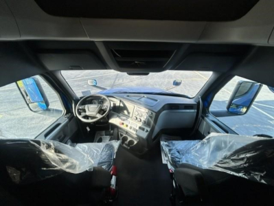 Freightliner Cascadia cab interior view with steering wheel, dashboard, and seats covered in plastic. Visible text on dashboard includes control panels and gauges.