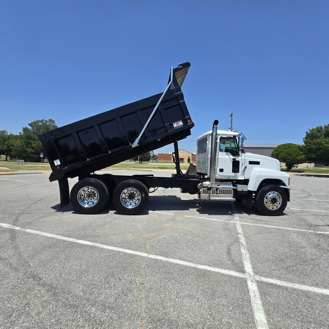 Dump truck side view showing a white Mack PI64 with a raised black dump body.