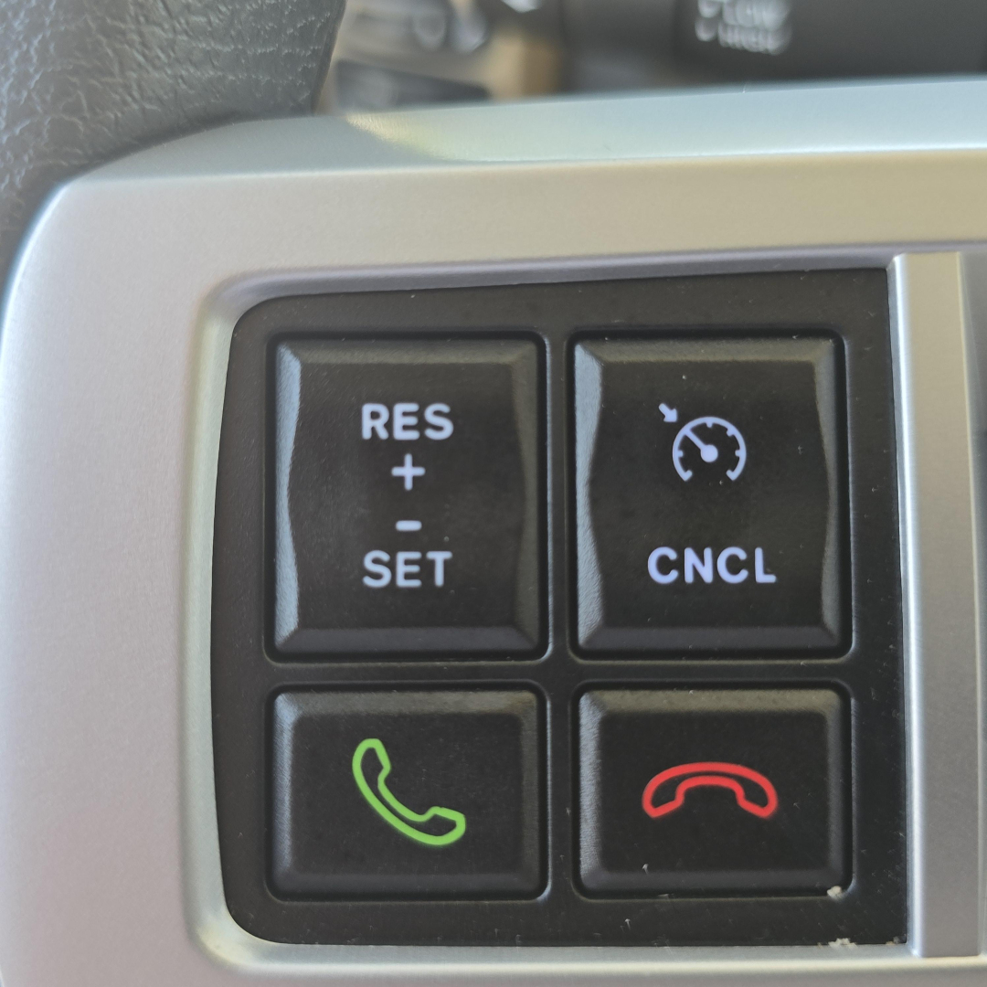 Truck cab interior control panel showing cruise control buttons and phone/hang-up icons on the steering column for a Mack PI64.