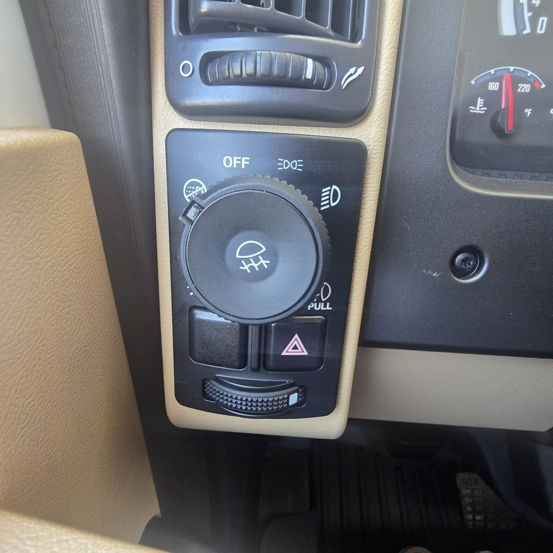 Dashboard and controls of a 2026 Mack PI64 showing a large circular headlight/auxiliary switch with OFF position, hazard switch, and climate vent above.