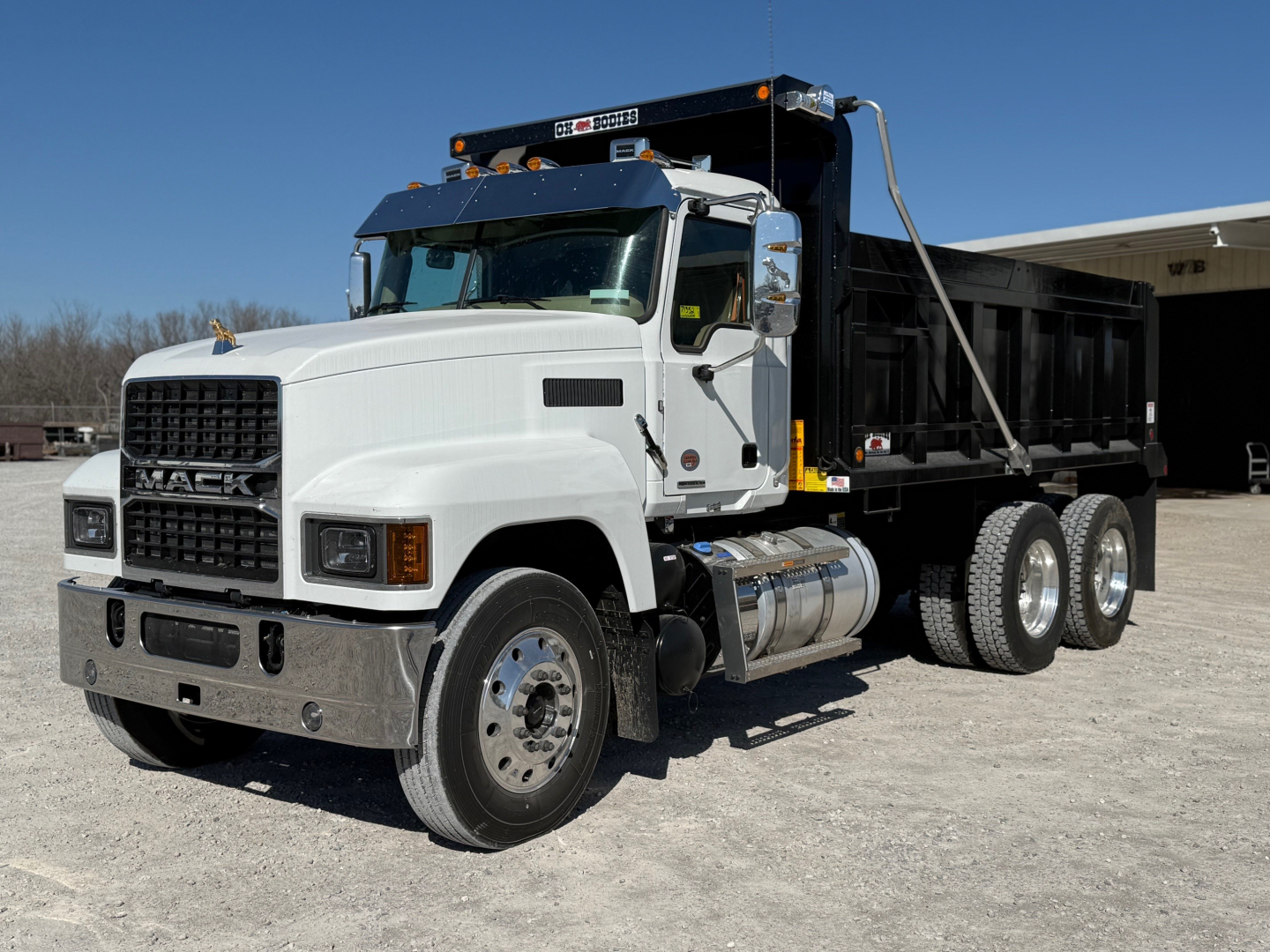 Dump truck in a white Mack PI64 cab with black dump body, front grille, dual rear wheels, and chrome bumper. View shows side profile and front-left angle.