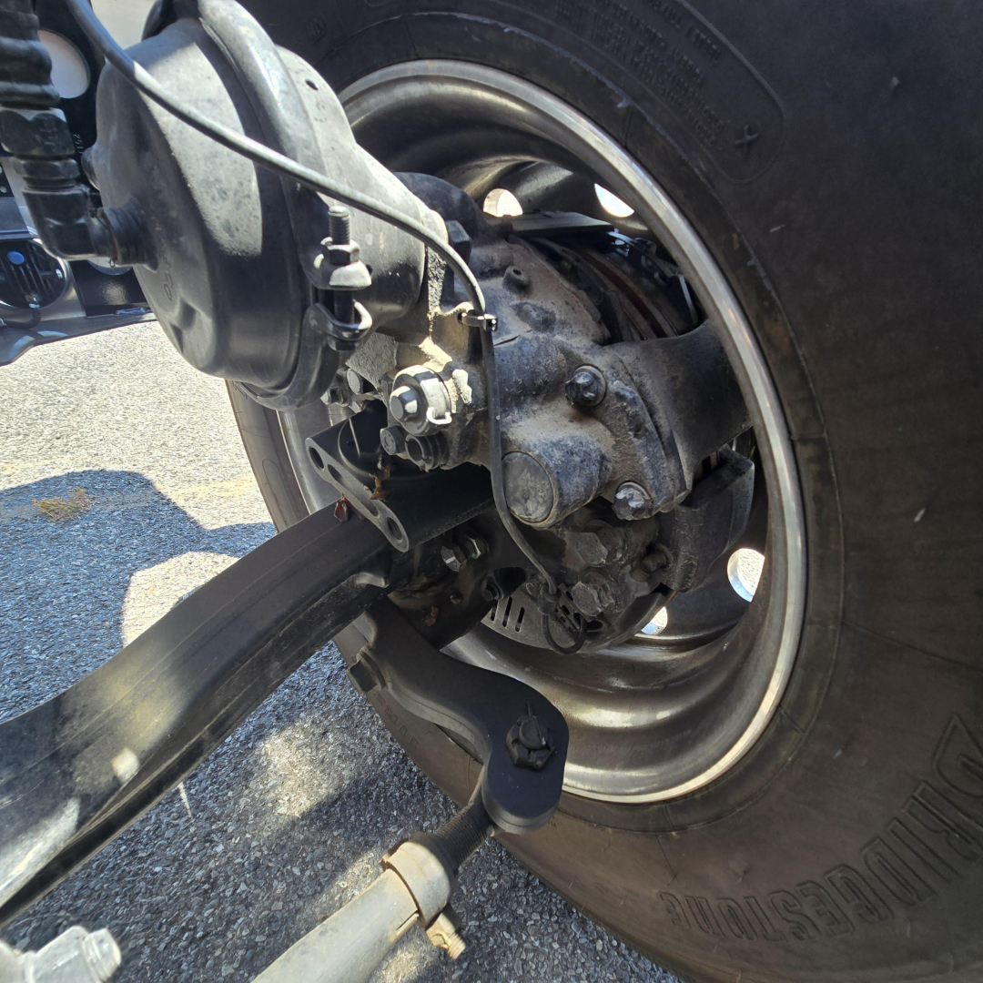 Front rear suspension hub and drive axle of a Mack PI64 dump truck showing wheel, brake drum, axle housing, and suspension link.