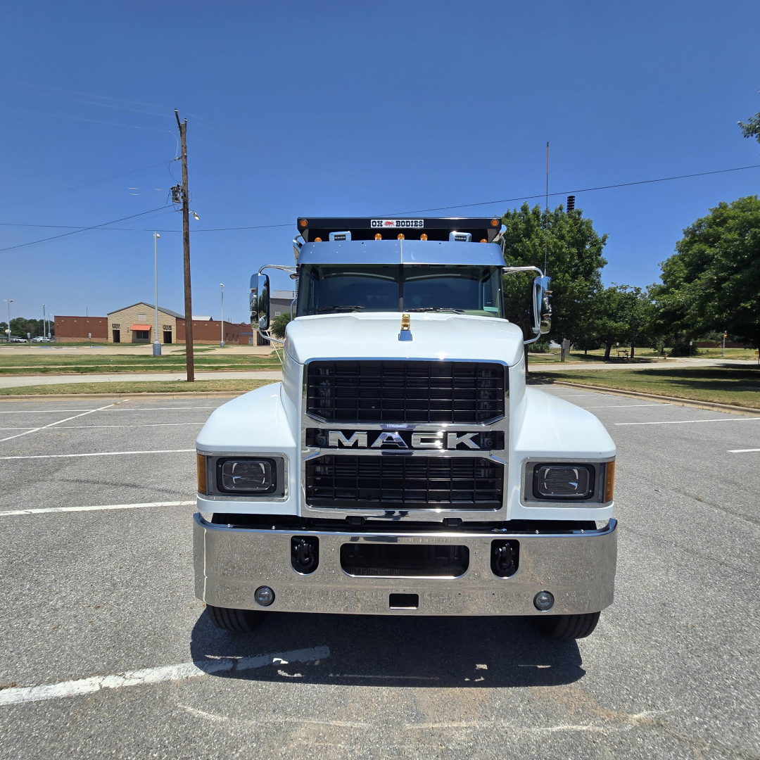 Front view of a white 2026 Mack PI64 dump truck showing large grille with MACK emblem and bumper, clear headlights, chrome bumper, and elevated cab.