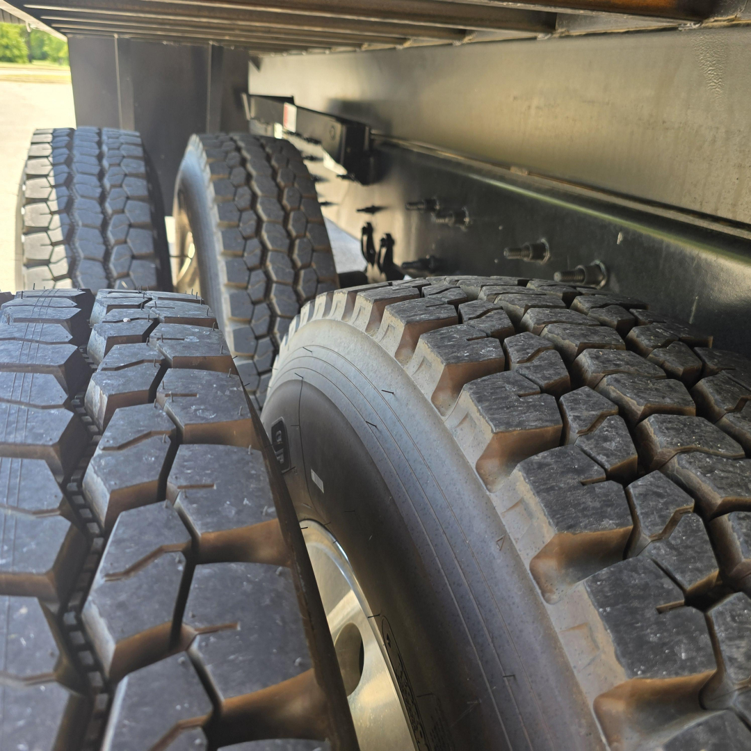 Truck wheel assembly and dual rear tires under a Mack PI64 trailer/tractor chassis showing treaded tires and undercarriage components.