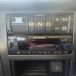 Mack PI64 dash showing R N D gear selector with + and - buttons and Drive Mode, and a Mack radio head unit.