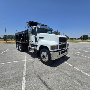 Mack PI64 dump truck in a parking lot, front-left view, white cab, black dump bed, chrome bumper, no visible text except Mack grille.