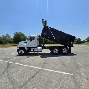 Mack PI64 dump truck with dumping bed raised, side view showing cab, dual rear axles, and black dump body.