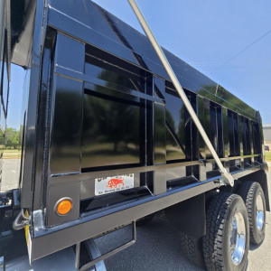 Dump truck bed side showing reinforced steel panels and wheel set with reflective tape and orange marker light.