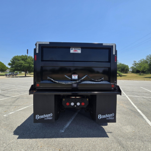 Dump truck bed of a new Mack PI64 dump with rear view, showing tailgate, illuminated brake lights, mud flaps labeled Bruckner’s Equipment, and a spare chain harness.