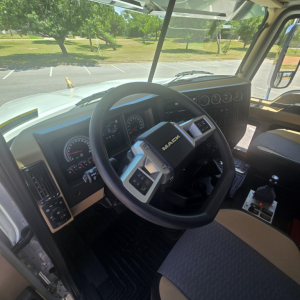 Cab interior of Mack PI64 left-hand drive showing steering wheel and instrument cluster with Mack branding on the center pad.